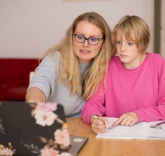 woman sits at table with girl helping her to study